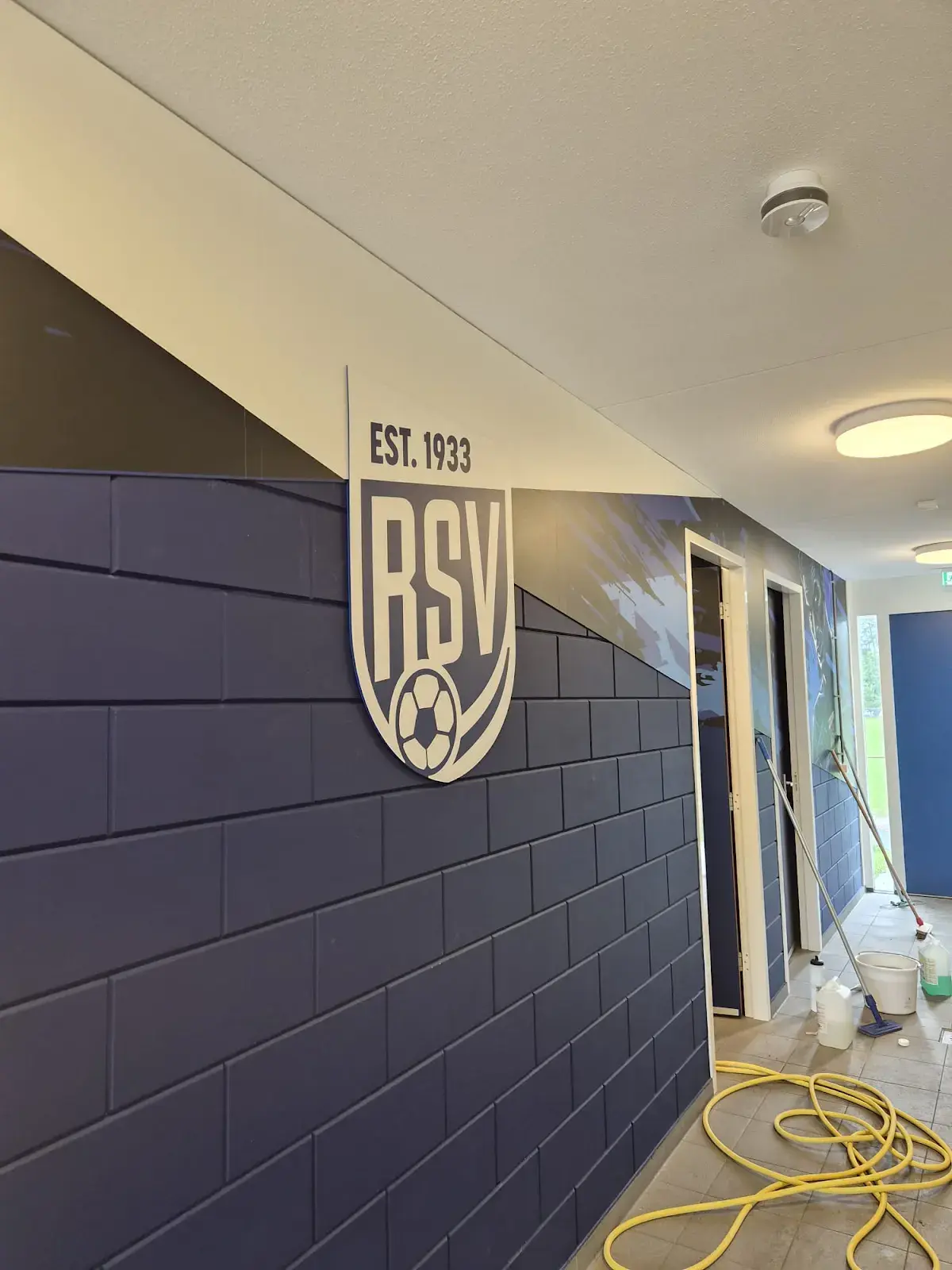 RSV-logo op de blauw-witte wand in de gang bij de kleedkamers.
